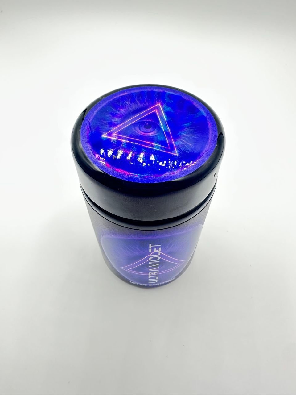Top lid of ULTRAVIOLET By DOJA jar featuring glowing purple eye inside neon triangle design